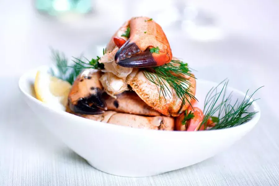 Crab legs are stacked in a white bowl and sprinkled with fresh dill.